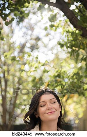 Stock Photography - Caucasian woman with eyes closed under tree. Fotosearch