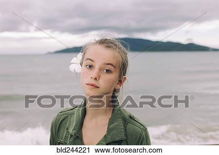 Stock Image - Caucasian woman with flower in hair near ocean. Fotosearch