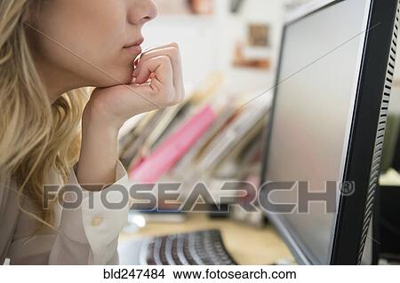 Picture - Caucasian woman with hand on chin reading computer. Fotosearch