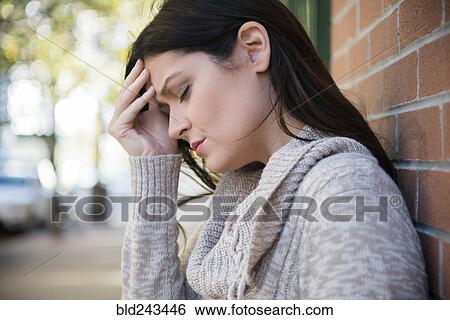 Stock Photograph - Caucasian woman with headache leaning on brick wall. Fotosearch