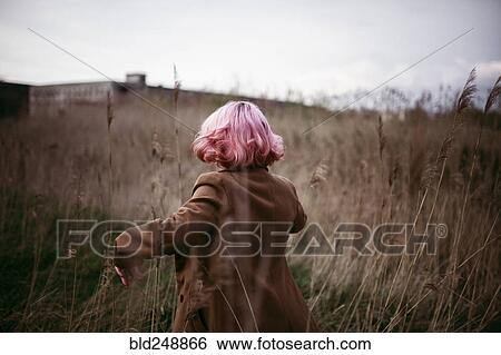 Stock Photograph - Caucasian woman with pink hair running in field. Fotosearch