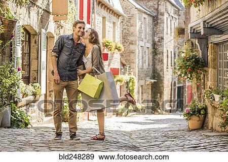 Stock Photo - Caucasian woman with shopping bags kissing man in city. Fotosearch