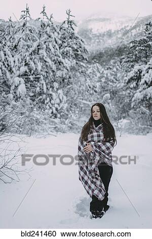 Stock Image - Caucasian woman wrapped in blanket in snowy forest. Fotosearch