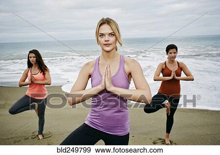 Stock Photo - Caucasian women performing yoga on beach. Fotosearch