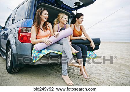 Stock Image - Caucasian women sitting in hatch of car on beach. Fotosearch