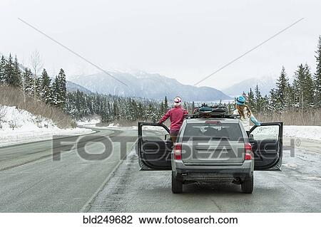 Stock Image - Caucasian women standing in car in winter admiring scenic view. Fotosearch