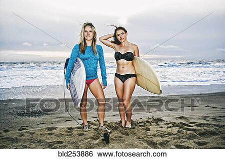 Caucasian women standing on beach holding surfboards View Large Photo Image Stock Photograph - Caucasian women standing on beach holding surfboards. Fotosearch