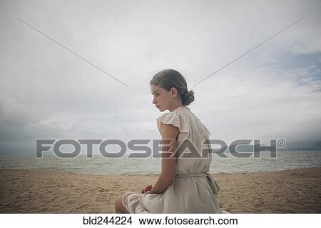 Picture - Caucasian women wearing dress sitting on beach. Fotosearch