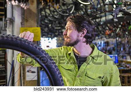 Stock Image - Caucasian worker repairing bicycle wheel in shop. Fotosearch