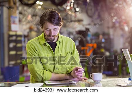 Stock Photo - Caucasian worker using digital tablet in bicycle shop. Fotosearch
