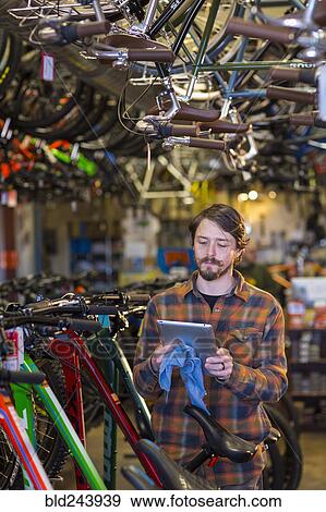 Stock Photo - Caucasian worker using digital tablet in bicycle shop. Fotosearch
