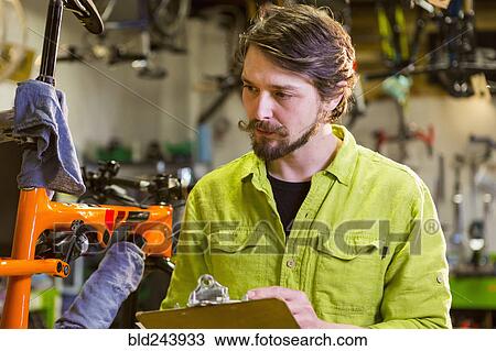 Stock Image - Caucasian worker writing on clipboard in bicycle shop. Fotosearch