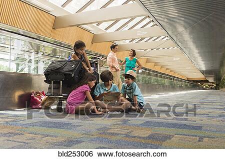 Stock Photograph - Children waiting in airport with family and using digital tablet. Fotosearch