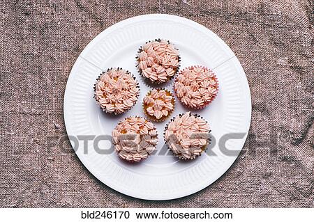 Stock Image - Close up of cupcakes with pink frosting on plate. Fotosearch