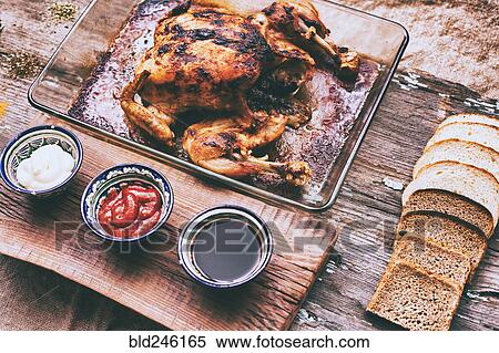 Stock Photography - Close up of roasted chicken with bread and sauces on wooden table. Fotosearch