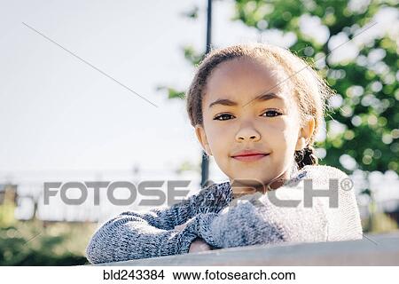 Picture - Confident Mixed Race girl leaning on wooden railing. Fotosearch