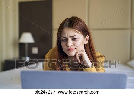 Stock Photo - Confused Caucasian woman laying on bed using laptop. Fotosearch