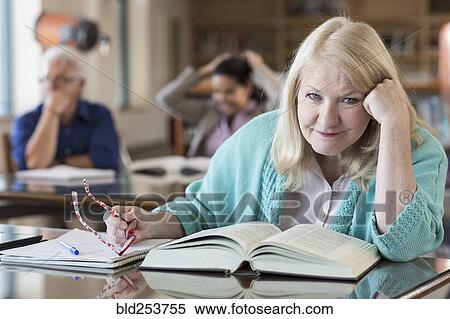 Stock Photography - Confused older woman reading book in library. Fotosearch