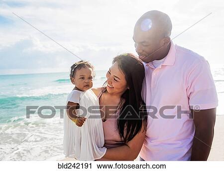 Stock Image - Couple admiring baby daughter on beach. Fotosearch