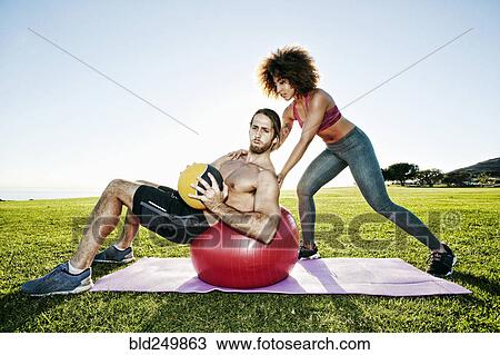 Stock Image - Couple exercising with fitness ball and heavy ball in sunny field. Fotosearch