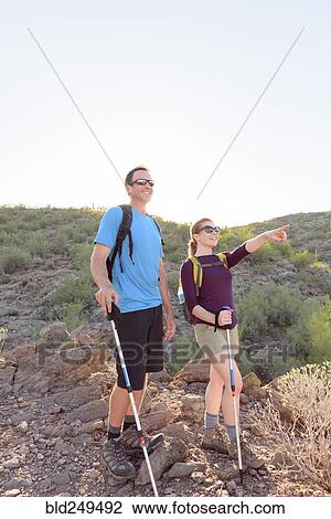 Stock Image - Couple hiking on hill holding walking sticks. Fotosearch