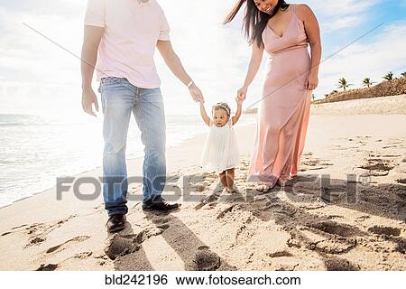 Couple holding hands of baby daughter walking on beach View Large Photo Image Stock Photograph - Couple holding hands of baby daughter walking on beach. Fotosearch