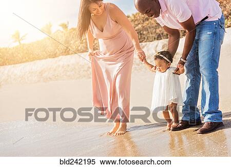 Stock Photography - Couple holding hands of baby daughter walking on beach. Fotosearch