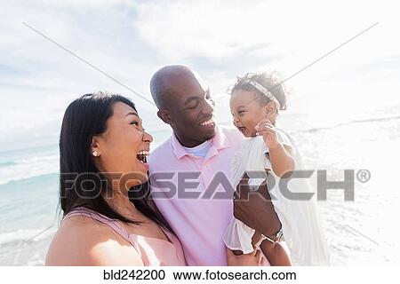 Couple laughing with baby daughter near ocean View Large Photo Image Stock Image - Couple laughing with baby daughter near ocean. Fotosearch