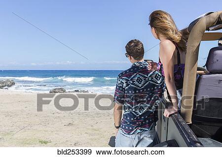 Stock Photo - Couple leaning on convertible car at beach. Fotosearch