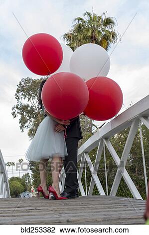 Stock Image - Couple on bridge kissing behind balloons. Fotosearch