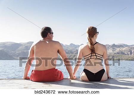 Stock Image - Couple sitting on dock at river. Fotosearch