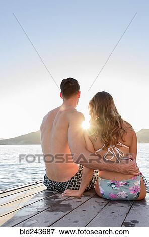 Stock Photo - Couple sitting on dock at river. Fotosearch