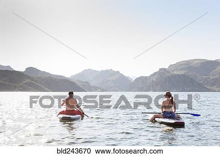 Stock Image - Couple sitting on paddleboards in river. Fotosearch