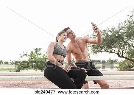 Stock Photo - Couple sitting on railing posing for cell phone selfie. Fotosearch