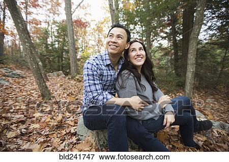 Stock Photo - Couple sitting on rock in forest during autumn. Fotosearch