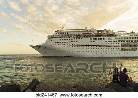Stock Photo - Couple sitting on rocks at river waving to cruise ship. Fotosearch