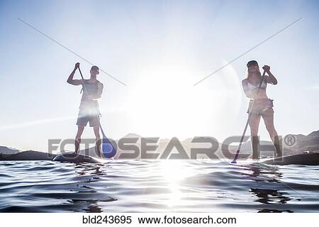 Stock Photography - Couple standing on paddleboards in river. Fotosearch
