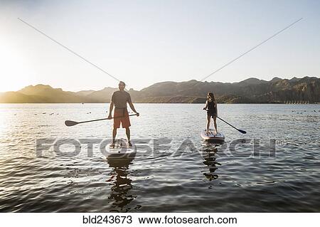 Stock Image - Couple standing on paddleboards in rover. Fotosearch