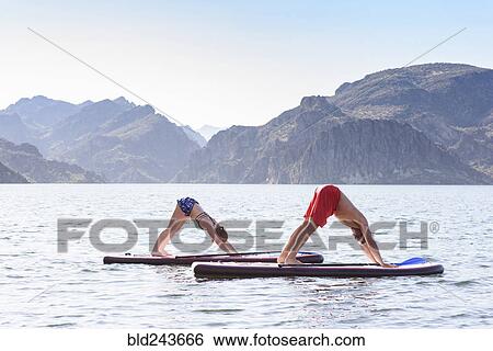 Couple stretching on paddleboards in river View Large Photo Image Stock Photograph - Couple stretching on paddleboards in river. Fotosearch