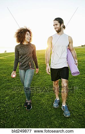 Stock Photo - Couple walking in sunny field carrying exercise mat. Fotosearch