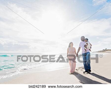 Stock Photo - Couple walking on beach with baby daughter. Fotosearch