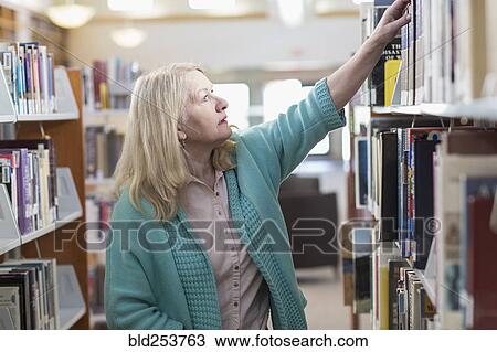 Curious Caucasian woman reaching for book in library View Large Photo Image Stock Image - Curious Caucasian woman reaching for book in library. Fotosearch