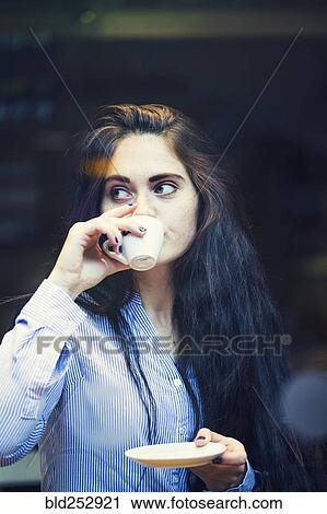 Stock Image - Curious Caucasian woman sipping coffee outdoors. Fotosearch
