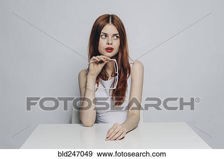 Curious Caucasian woman sitting at table holding white eyeglasses View Large Photo Image Stock Photo - Curious Caucasian woman sitting at table holding white eyeglasses. Fotosearch