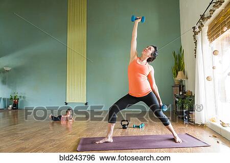 Stock Photograph - Daughter watching Mixed Race expectant mother lifting weights. Fotosearch