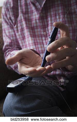 Stock Photo - Diabetic Hispanic man checking blood in finger. Fotosearch