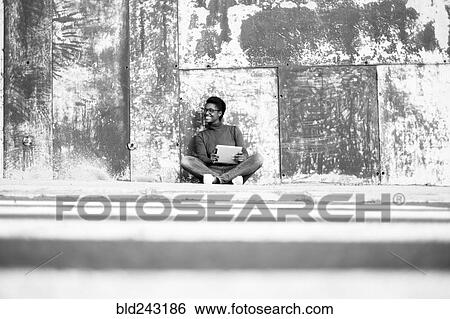 Stock Photograph - Distant African American woman sitting on ground using digital tablet. Fotosearch