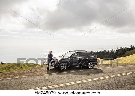 Stock Photo - Distant Caucasian businessman leaning on car. Fotosearch