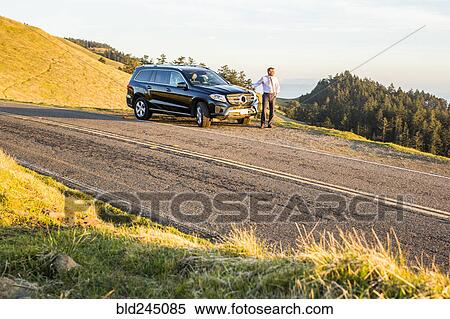 Stock Photography - Distant Caucasian businessman leaning on car. Fotosearch