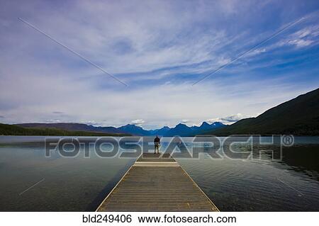 Stock Photograph - Distant Caucasian man standing on dock at lake. Fotosearch